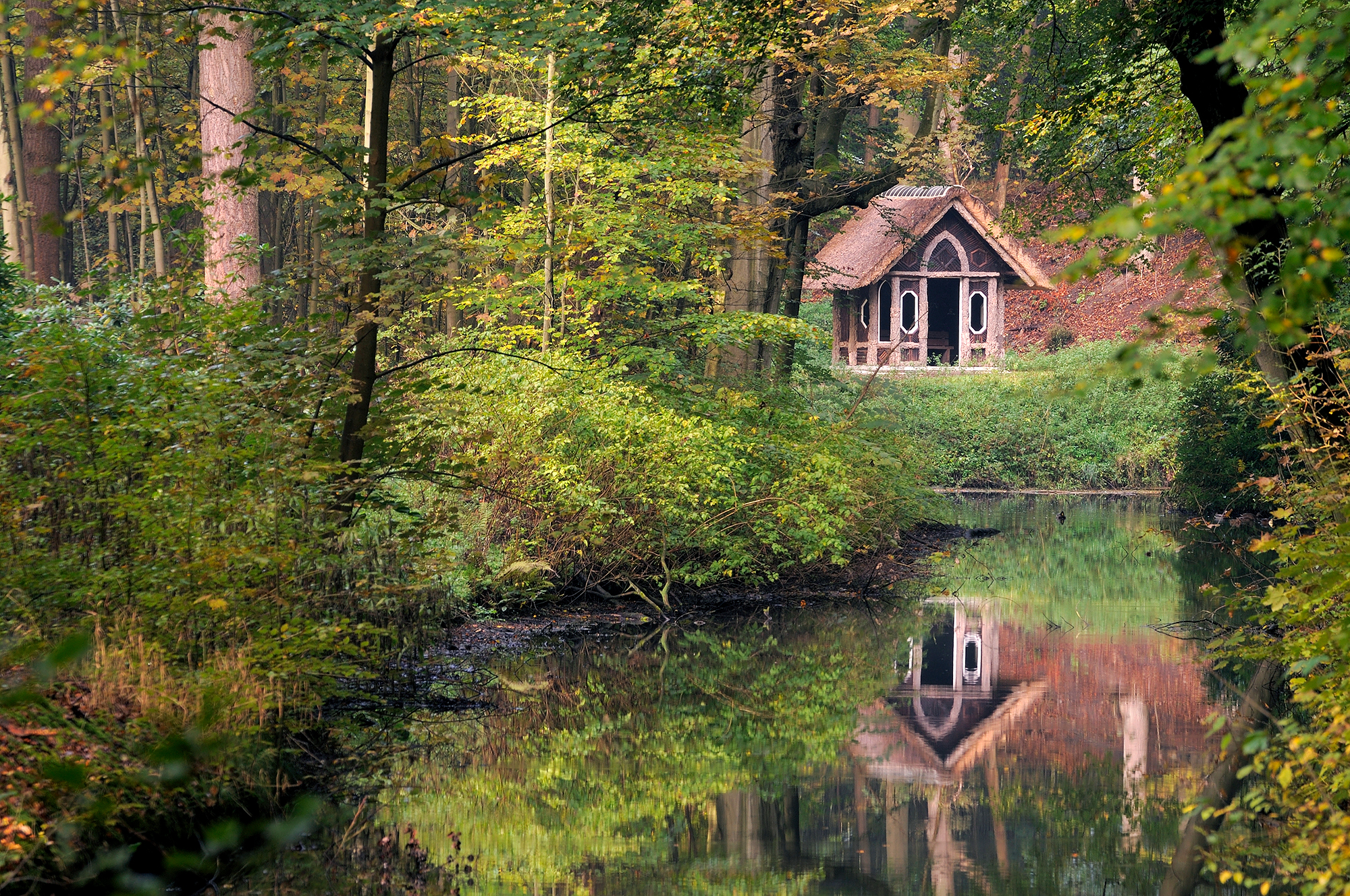Doorkijkje naar een weerspiegeling van prieeltje in het water van beek tijdens de herfst op Landgoed Elswout in Overveen.