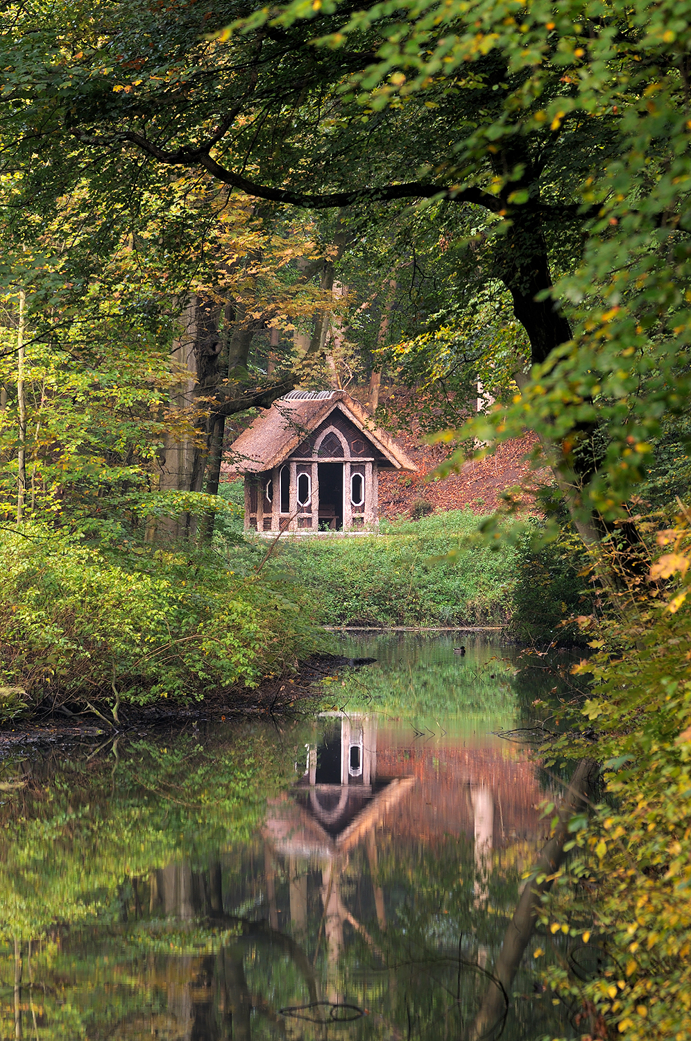 Doorkijkje naar een weerspiegeling van prieeltje in het water van beek tijdens de herfst op Landgoed Elswout in Overveen.