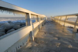 IJspegels hangen aan het hekwerk van een steiger met uitzicht op drijvende ijsschotsen tijdens winter op het IJsselmeer.