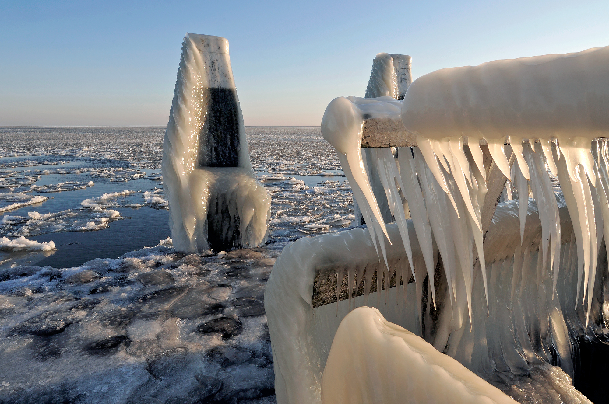 IJspegels hangen aan het hek van een bevroren steiger tijdens een koude winterdag op het IJsselmeer bij Den Oever.