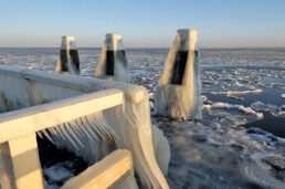 IJspegels hangen aan het hekwerk van een steiger met uitzicht op drijvende ijsschotsen tijdens winter op het IJsselmeer.