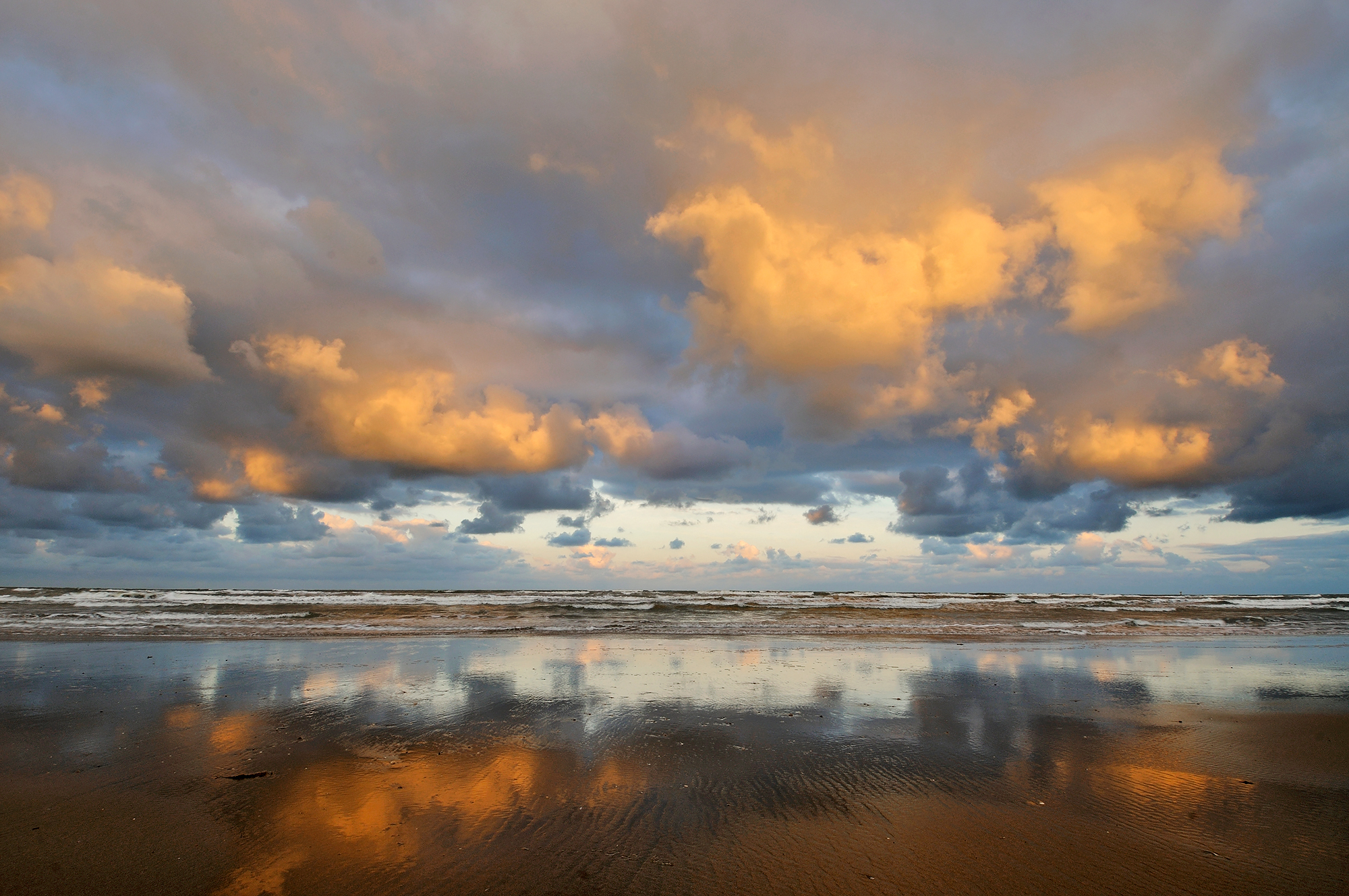 Warm licht van de zonsopkomst weerspiegelt op wolkenlucht boven zee op het Kennemerstrand bij IJmuiden.