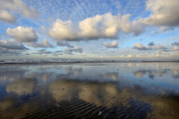Weerspiegeling van rij wolken in ondiep zeewater langs de vloedlijn op het strand van Wijk aan Zee