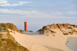 Warm zonlicht schijnt op zanderige duinhelling en rode vuurtoren Groote Kaap in de Noordduinen bij Julianadorp aan Zee.