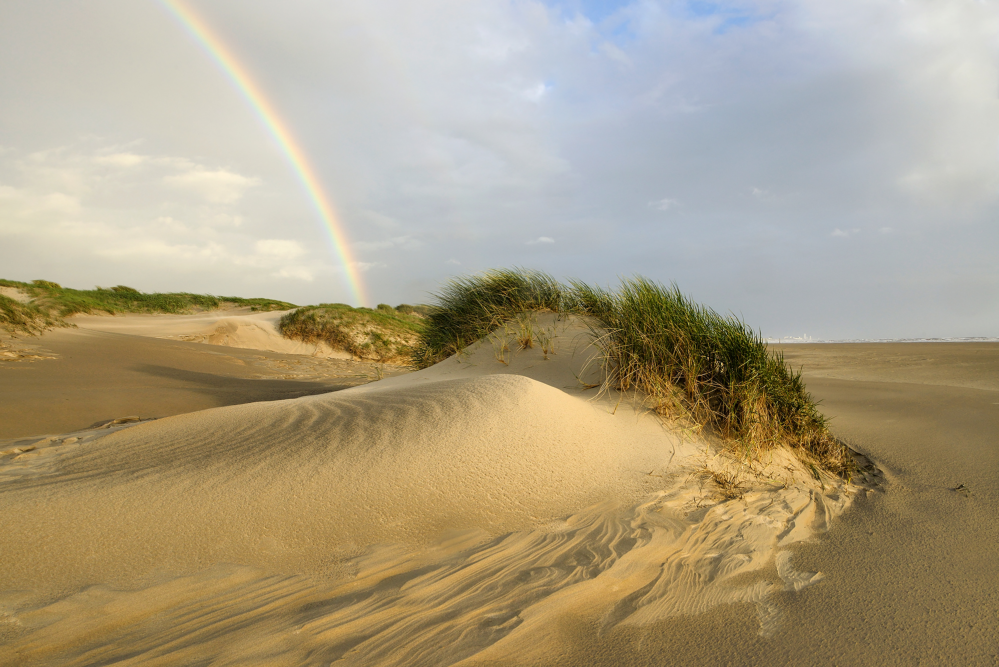 Regenboog boven het strand en de eerste rij zeeduinen na een regenbui op het Kennemerstrand bij IJmuiden.