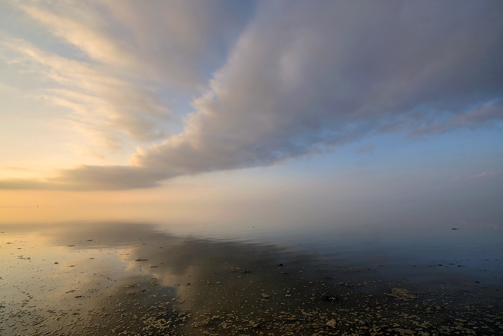 Weerspiegeling van wolkenlucht in het ondiepe water van de Waddenzee tijdens zonsondergang op Wieringen.