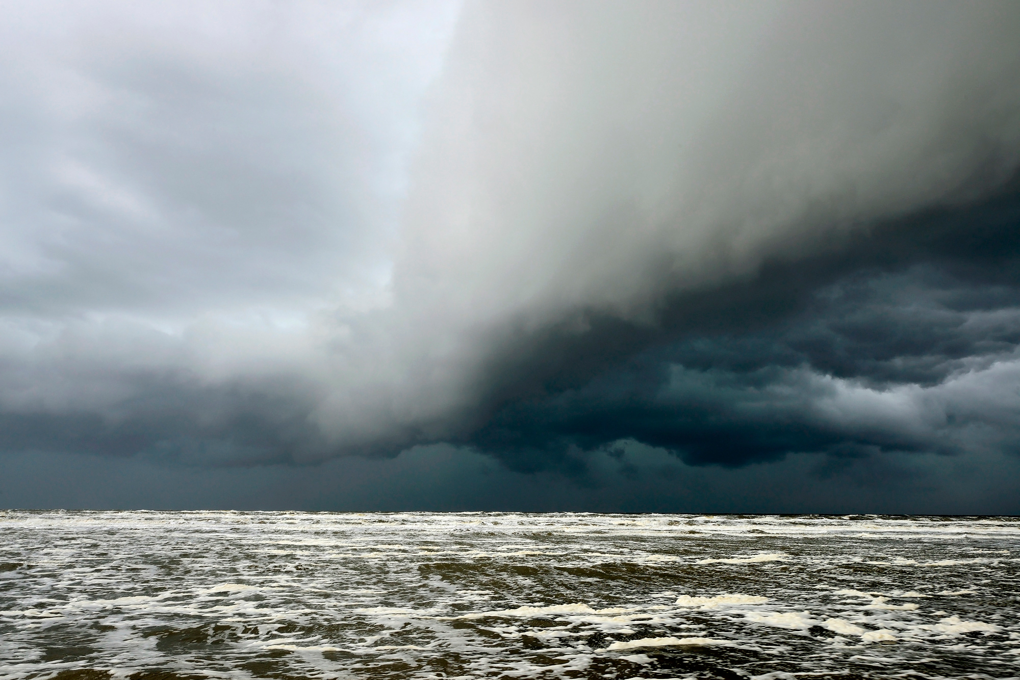 Donkere, dreigende wolkenlucht van hagelbui nadert vanaf zee het strand tijdens storm bij Castricum aan Zee.