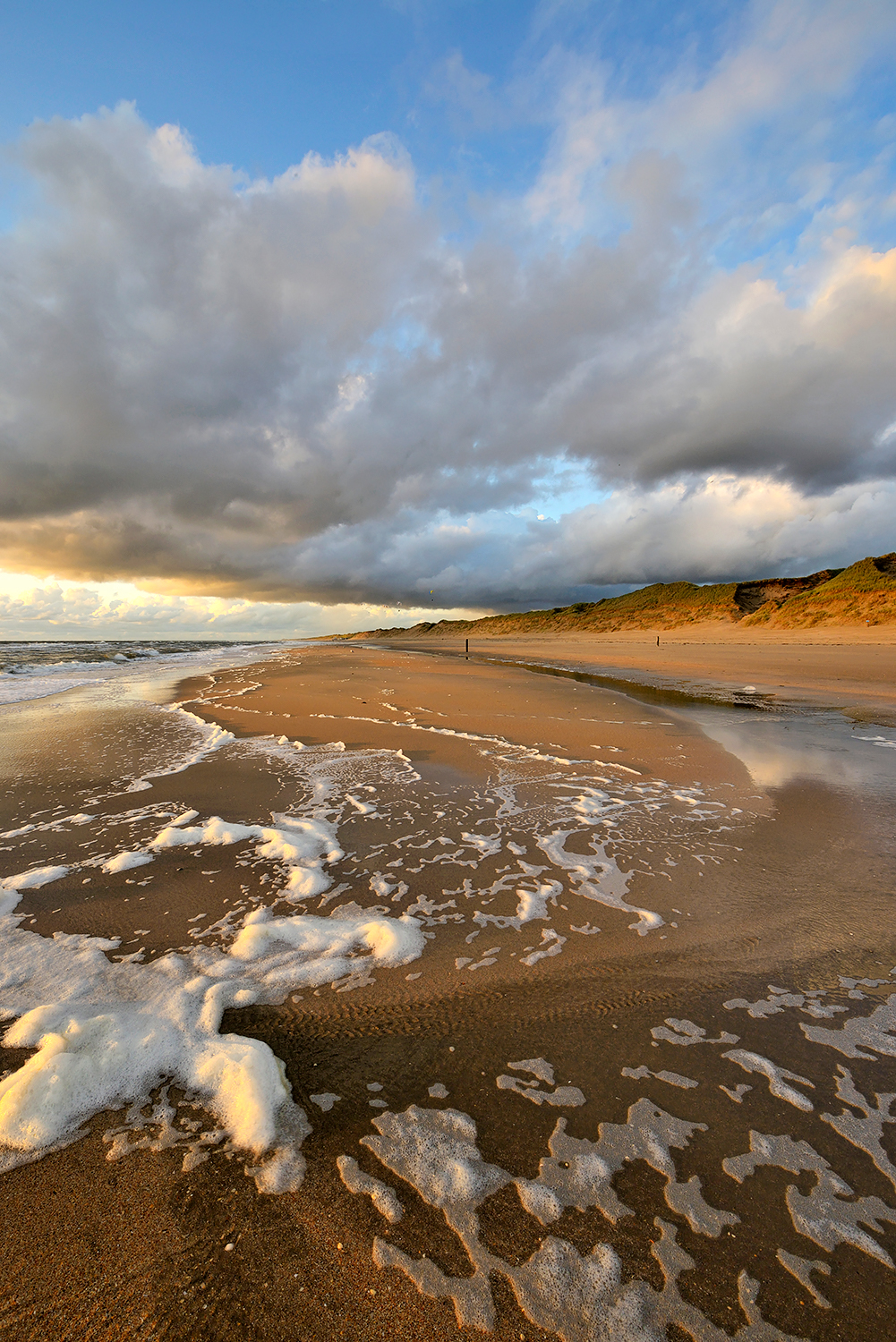 Warm licht van zonsondergang schijnt op wolkenlucht boven de zee en het strand van Heemskerk.
