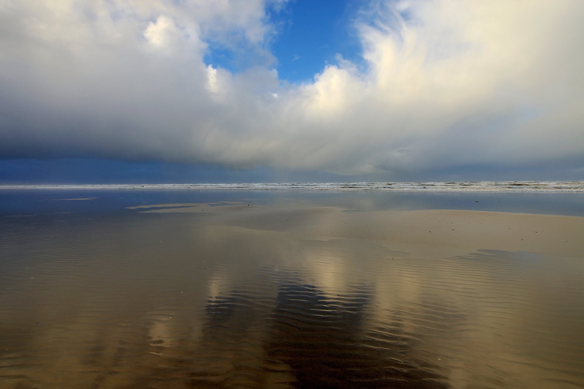Weerspiegeling van wolkenlucht boven zee in het ondiepe water langs de vloedlijn op het Kennemerstrand bij IJmuiden.