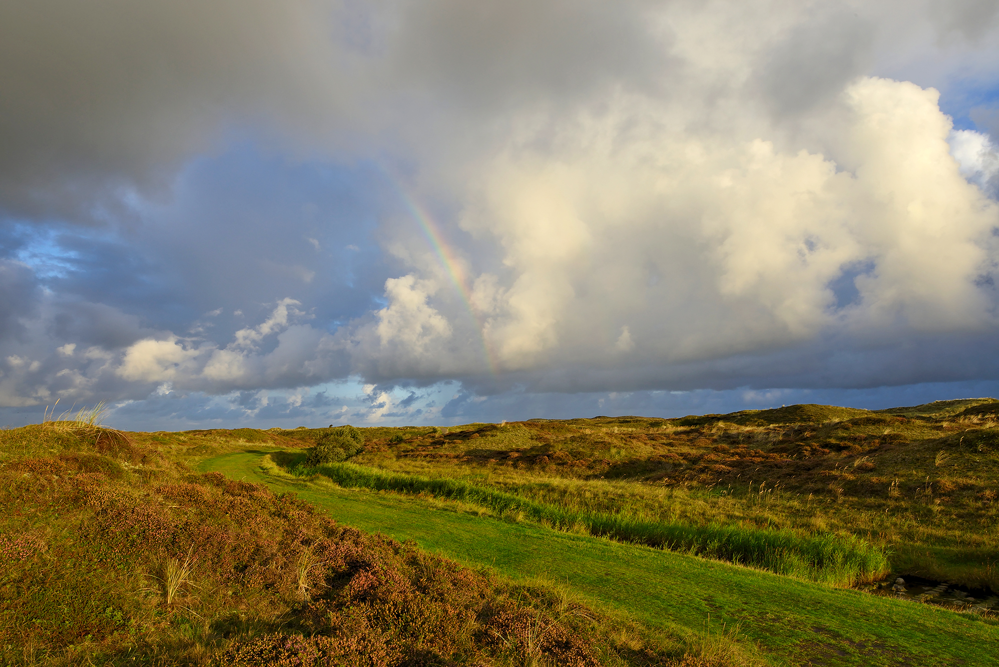 Wolken en regenboog boven wandelpad langs de Moksloot in het Nationaal Park Duinen van Texel bij Den Hoorn.