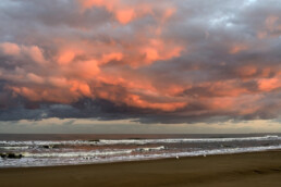 Warm, roze licht van de zon schijnt op een wolkenlucht boven zee tijdens zonsopkomst op het strand van Bloemendaal aan Zee
