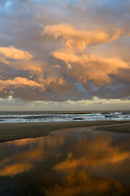 Warm, roze licht van de zon schijnt op een wolkenlucht boven zee tijdens zonsopkomst op het strand van Bloemendaal aan Zee