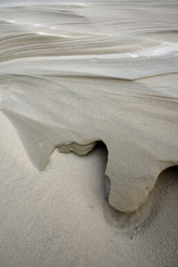 Door de wind uitgekerfde vormen en lijnen in het zand van de helmduinen na storm op het strand van Wijk aan Zee.