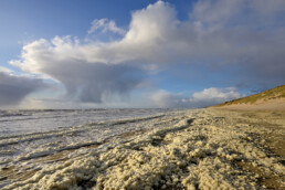 Regenbui en vlokken van aangespoeld schuimalg langs de vloedlijn tijdens storm op het strand van Wijk aan Zee.