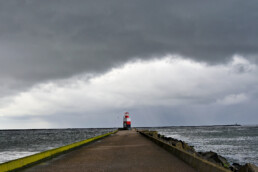 Donkere wolkenlucht van regenbui boven rood met wit gestreept lichthuis aan het einde van de Noordpier bij Wijk aan Zee.