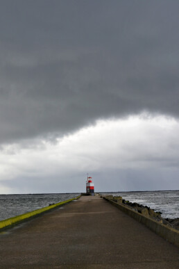 Donkere wolkenlucht van regenbui boven rood met wit gestreept lichthuis aan het einde van de Noordpier bij Wijk aan Zee.