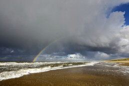 Regenboog aan de onderkant van een hagelbui op het strand van de Noordduinen bij Callantsoog