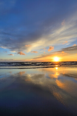 Warme gloed van zonsondergang weerspiegelt in het ondiepe zeewater langs de vloedlijn op het strand van Wijk aan Zee.