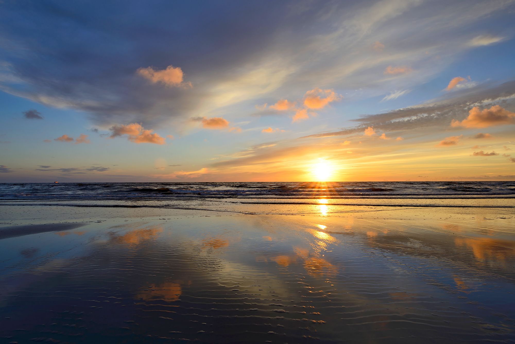 Warme gloed van zonsondergang weerspiegelt in het ondiepe zeewater langs de vloedlijn op het strand van Wijk aan Zee.