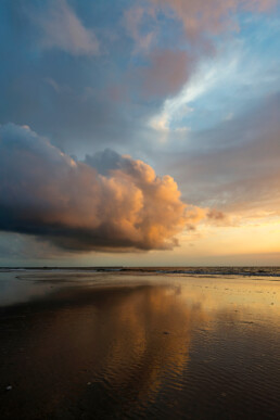 Warme gloed van ondergaande zon schijnt op wolken tijdens zonsondergang op het strand van Wijk aan Zee.