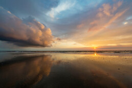 Warme gloed van ondergaande zon schijnt op wolken tijdens zonsondergang op het strand van Wijk aan Zee.