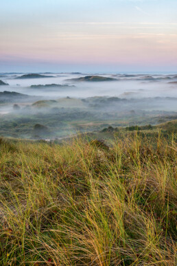 Uitzicht vanaf duintop over lagen mist tussen duinen tijdens zonsopkomst in het Noordhollands Duinreservaat bij Egmond aan Zee.