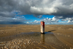 Donkere wolken boven een rood gekleurde houten strandpaal op de lege strandvlakte van De Hors op de zuidpunt van Waddeneiland Texel.