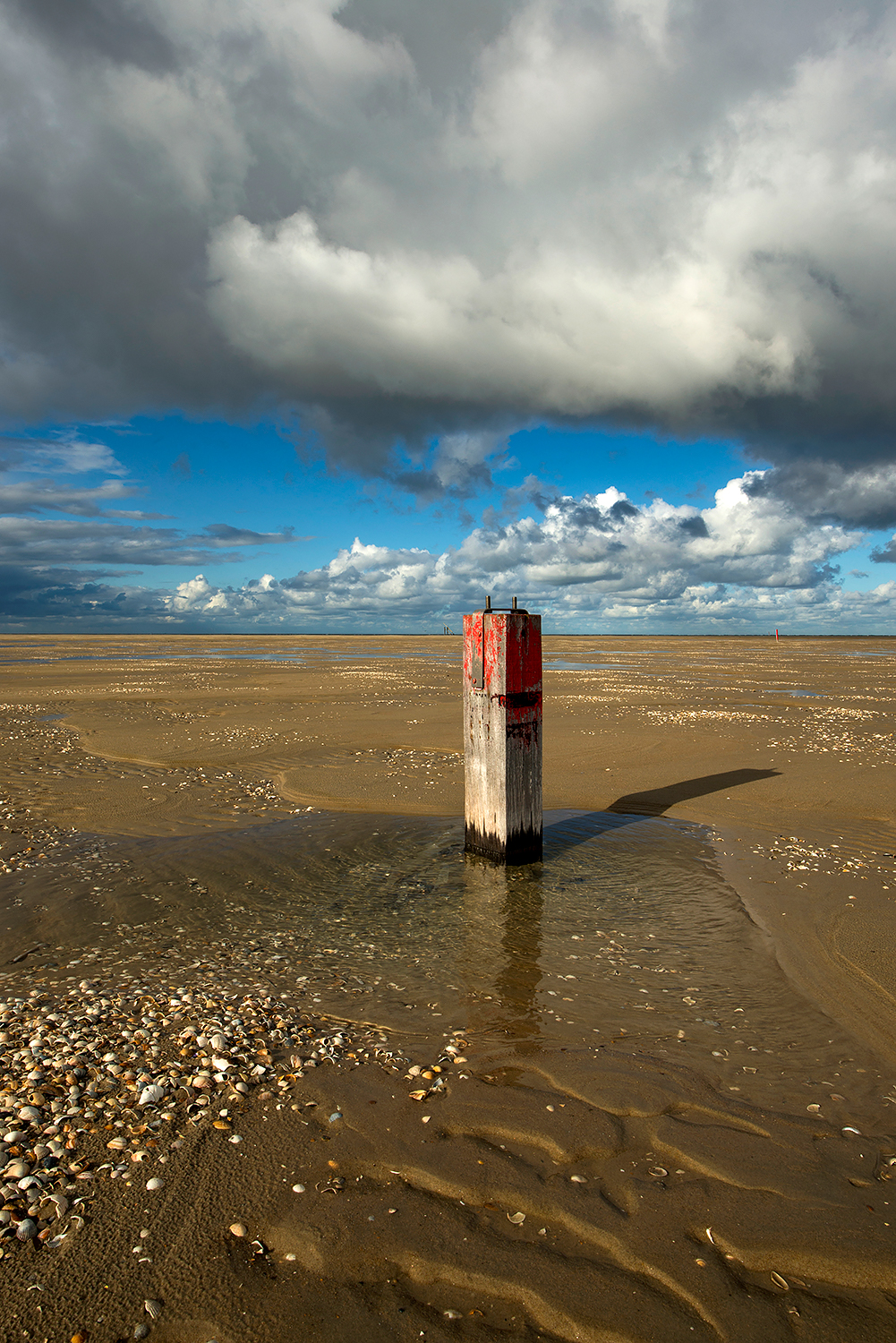 Donkere wolken boven een rood gekleurde houten strandpaal op de lege strandvlakte van De Hors op de zuidpunt van Waddeneiland Texel.