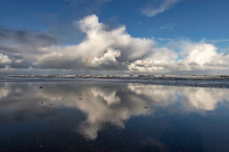 Weerspiegeling van wolkenlucht boven de Noordzee in het ondiepe zeewater langs de vloedlijn op het strand van Wijk aan Zee.