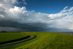 Grote wolkenlucht strekt zich uit boven de polders en dijk bij het dorpje Vatrop op het voormalige Waddeneiland Wieringen