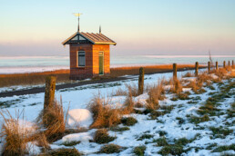 Warme gloed van zonsopkomst schijnt op peilschaalhuisje aan de rand van de Waddenzee op Wieringen