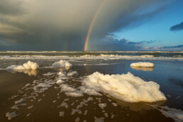 Regenboog en aangespoeld zeeschuim op het strand van Hargen aan Zee