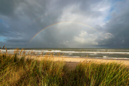 Uitzicht vanaf de duinen op het strand en een regenboog boven zee in het Noordhollands Duinreservaat bij Egmond-Binnen